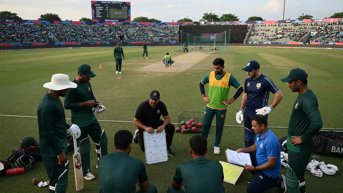 Players and coaches in mixed training kits gathered on a grass cricket field around a whiteboard diagram during daylight practice